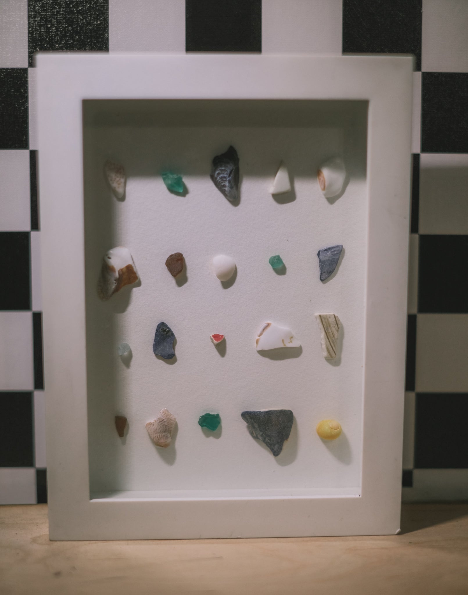 Framed display of small stones and pebbles on a checkered background