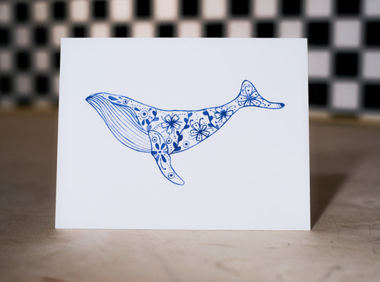 Card with a blue whale illustration on a white background, against a checkered wall.