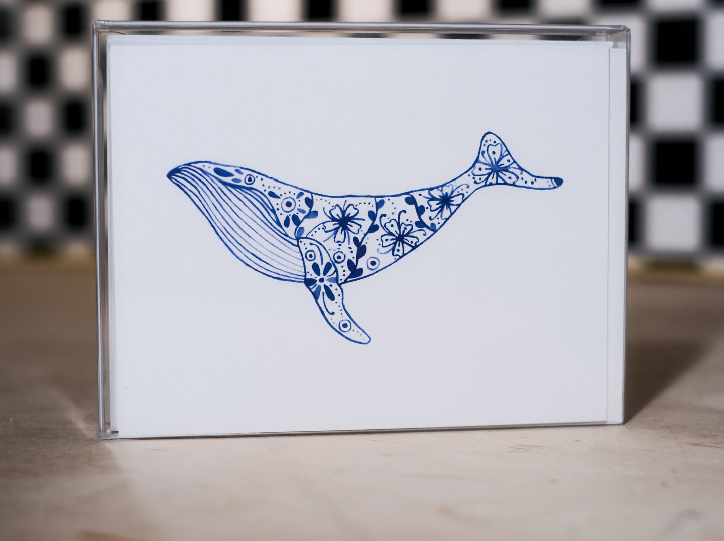 greeting card pack with a blue whale illustration design on a white background, against a black and white checkered wall.