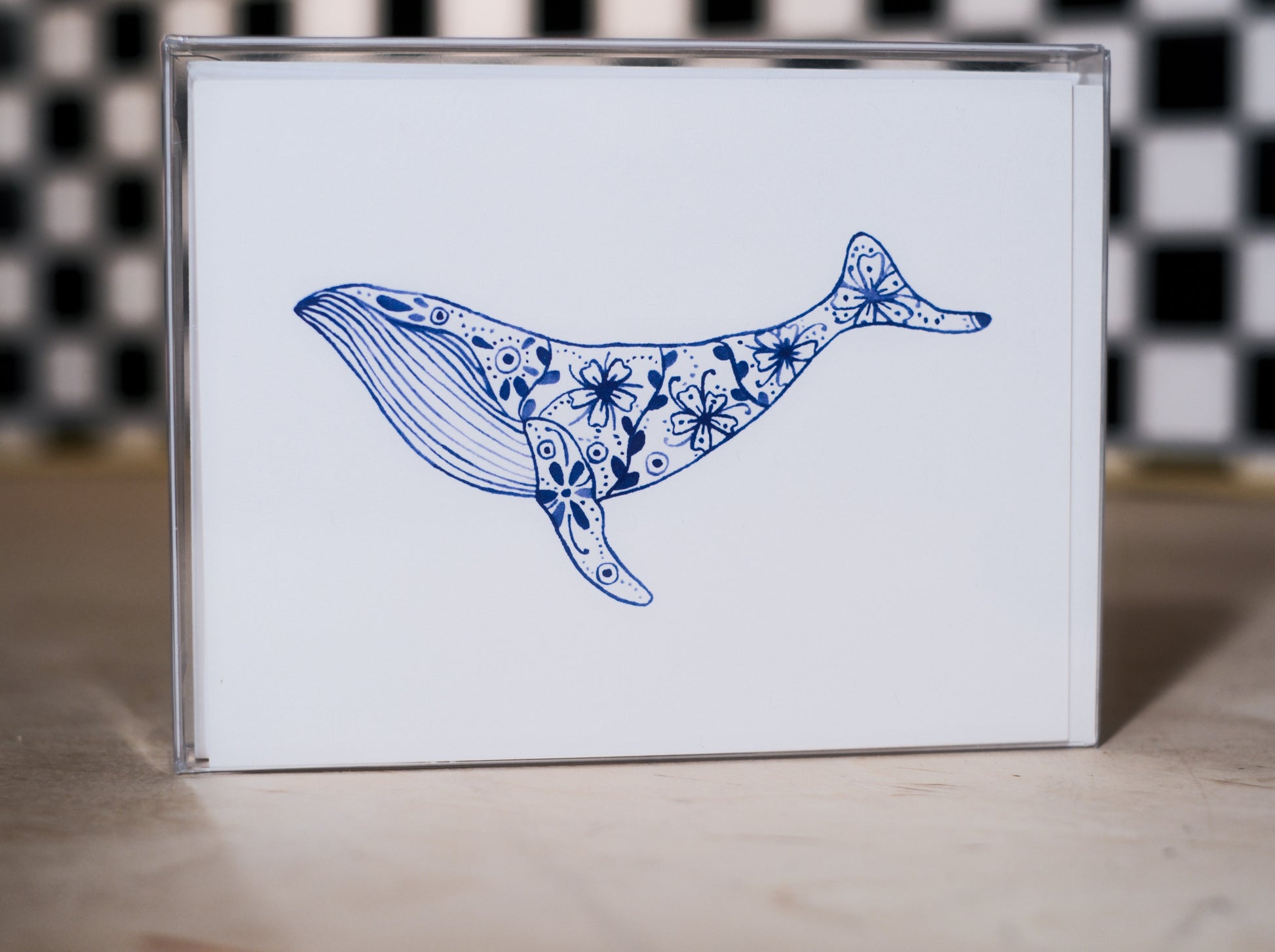 greeting card pack with a blue whale illustration design on a white background, against a black and white checkered wall.