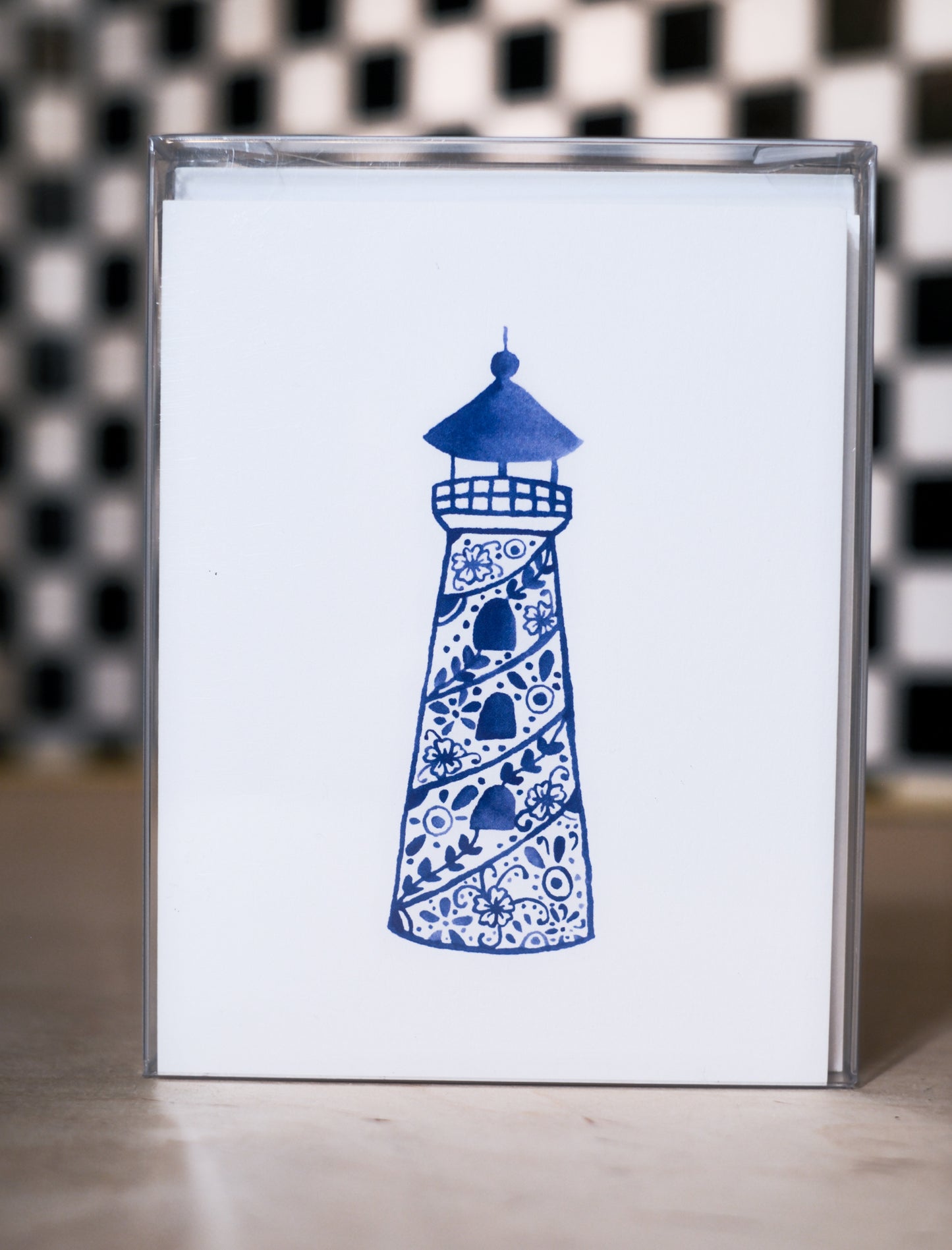 greeting card pack with a blue lighthouse design on a white background, against a black and white checkered wall.