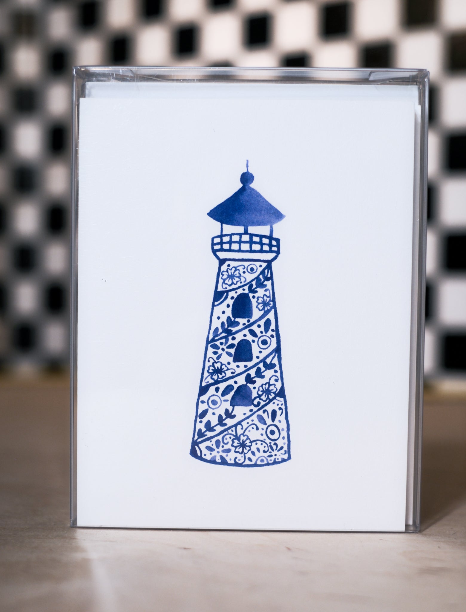 greeting card pack with a blue lighthouse design on a white background, against a black and white checkered wall.