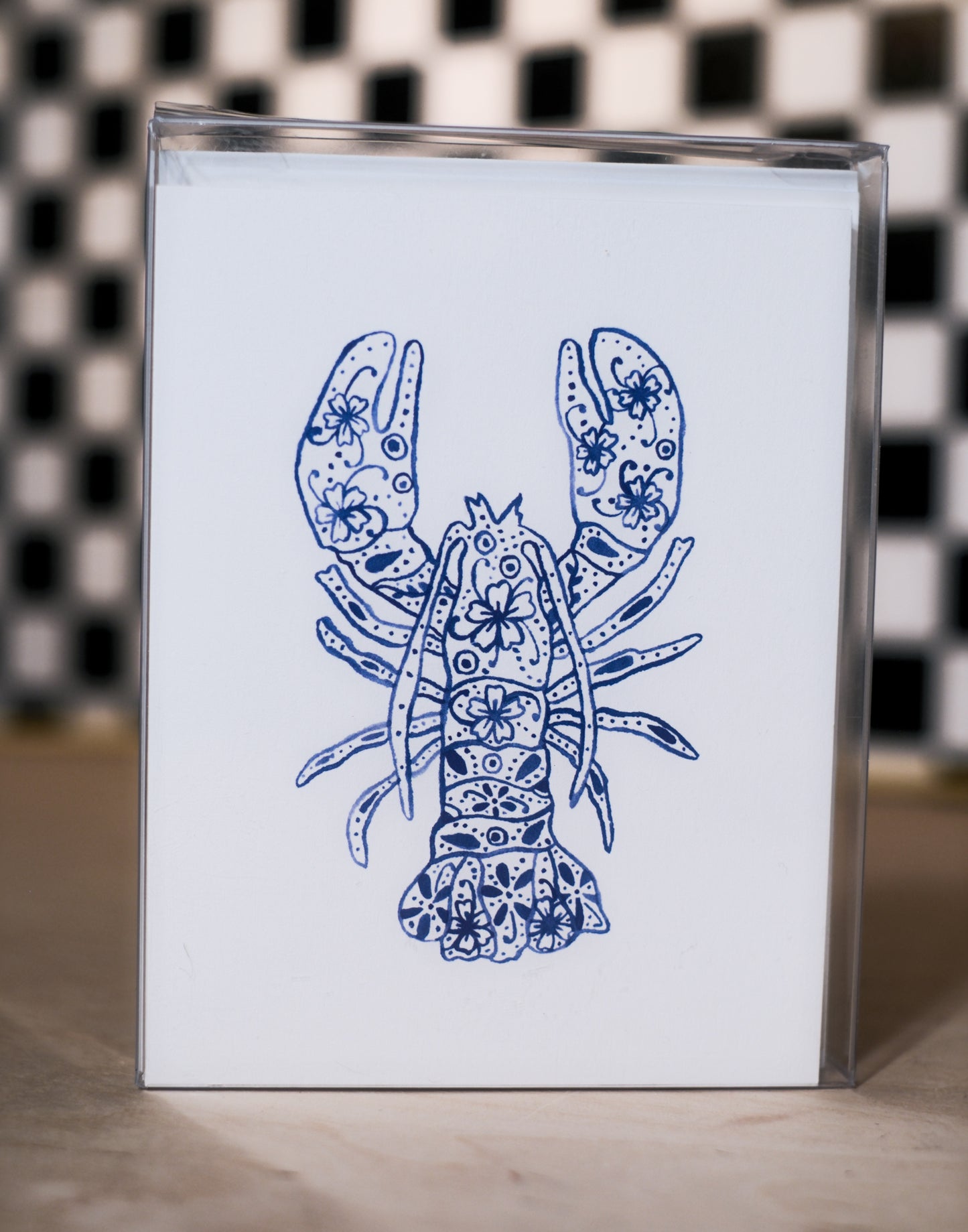 greeting card pack with a blue lobster design design on a white background, against a black and white checkered wall.