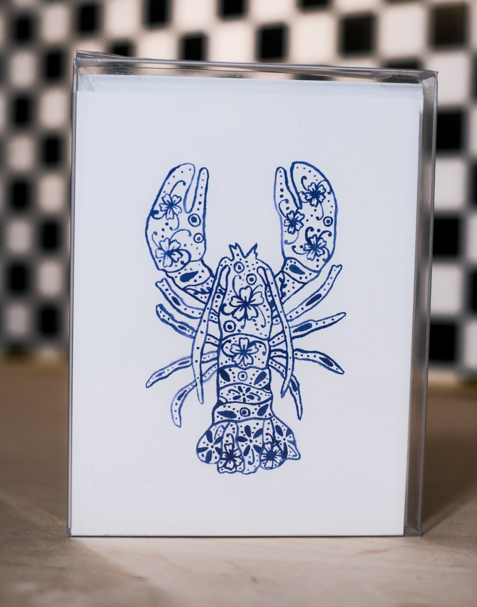 greeting card pack with a blue lobster design design on a white background, against a black and white checkered wall.