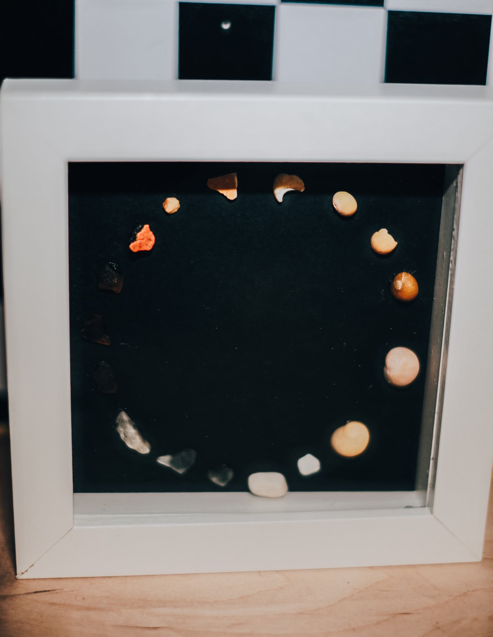 Decorative shadow box with pebbles arranged in a circular pattern on a dark background.