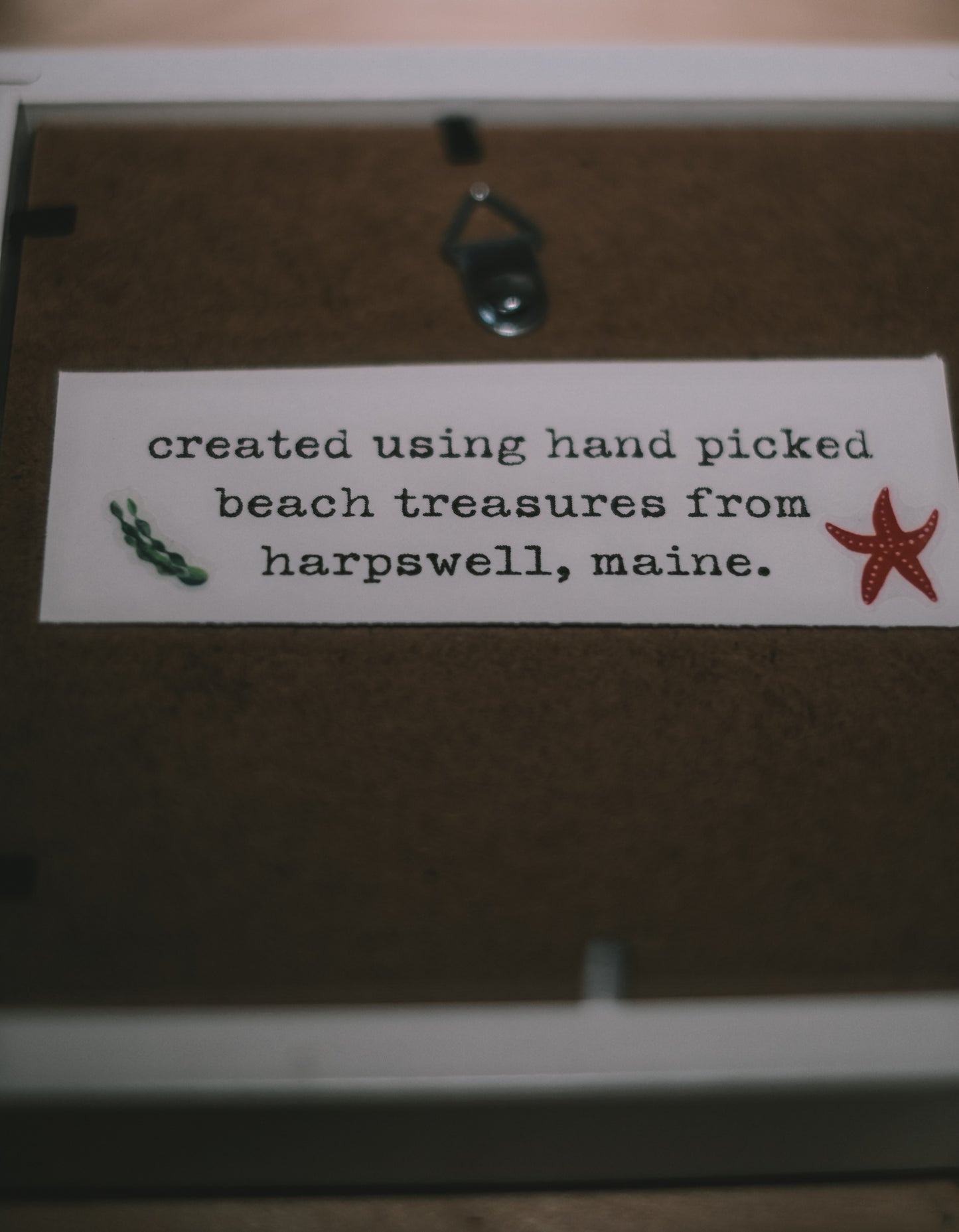 Label on a wooden surface with text 'created using hand picked beach treasures from harpswell, maine.'