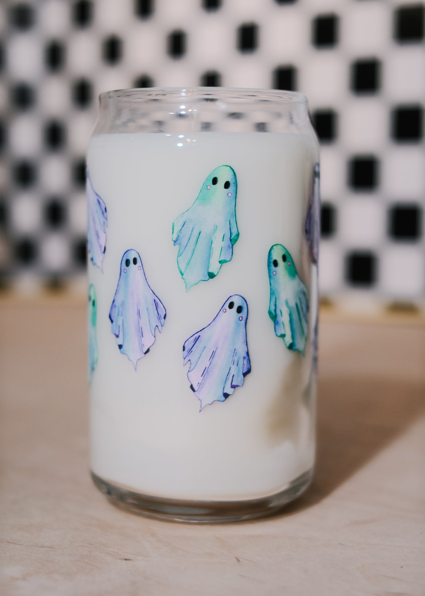 Glass tumbler filled with soy wax with ghost designs on a checkered background