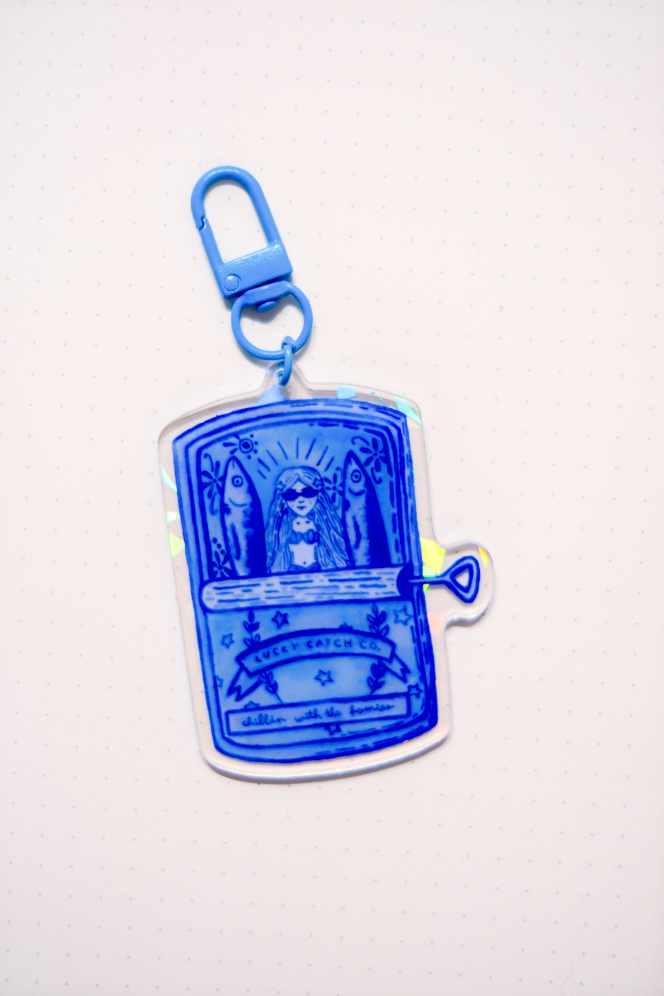 Blue keychain with a design of a mermaid and two fish in a tin can on a white background.