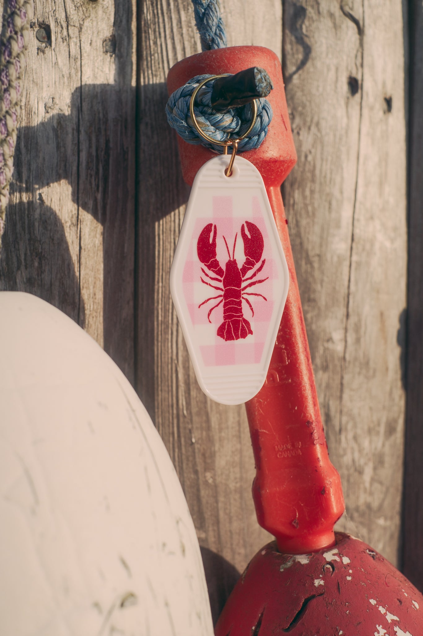 Red buoy with a white tag featuring a red lobster design, attached to a wooden post.