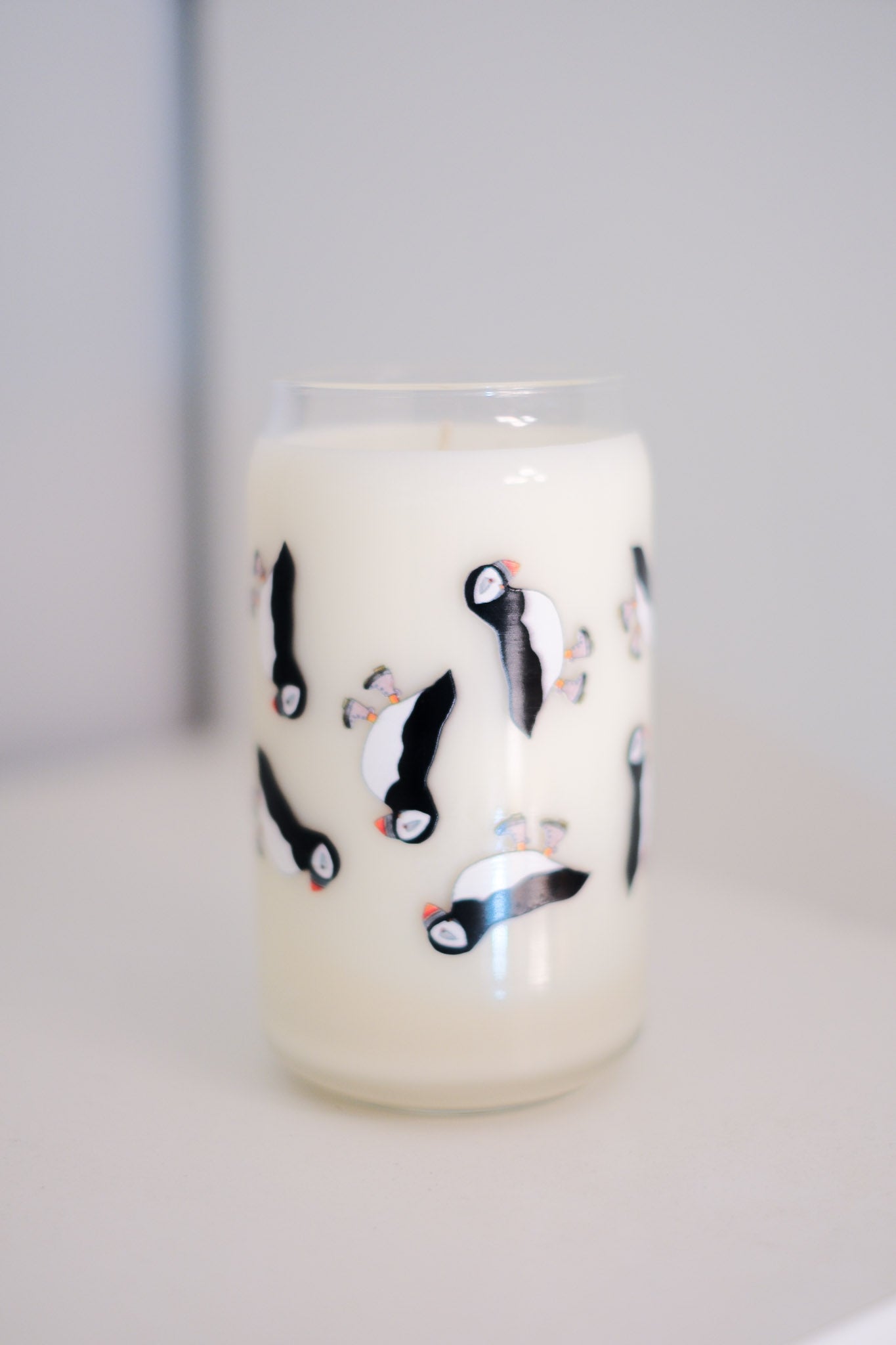 A clear glass candle with a pattern of puffin with brown boots on it.