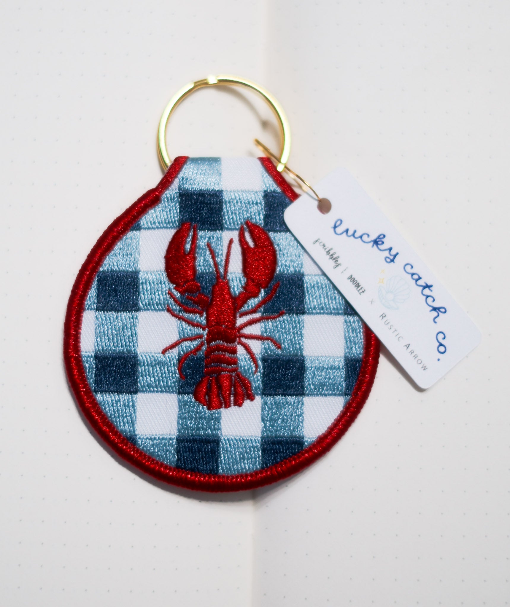 blue and white square pattern, with red lobster illustration patch fabric keychain, with gold keyring.
