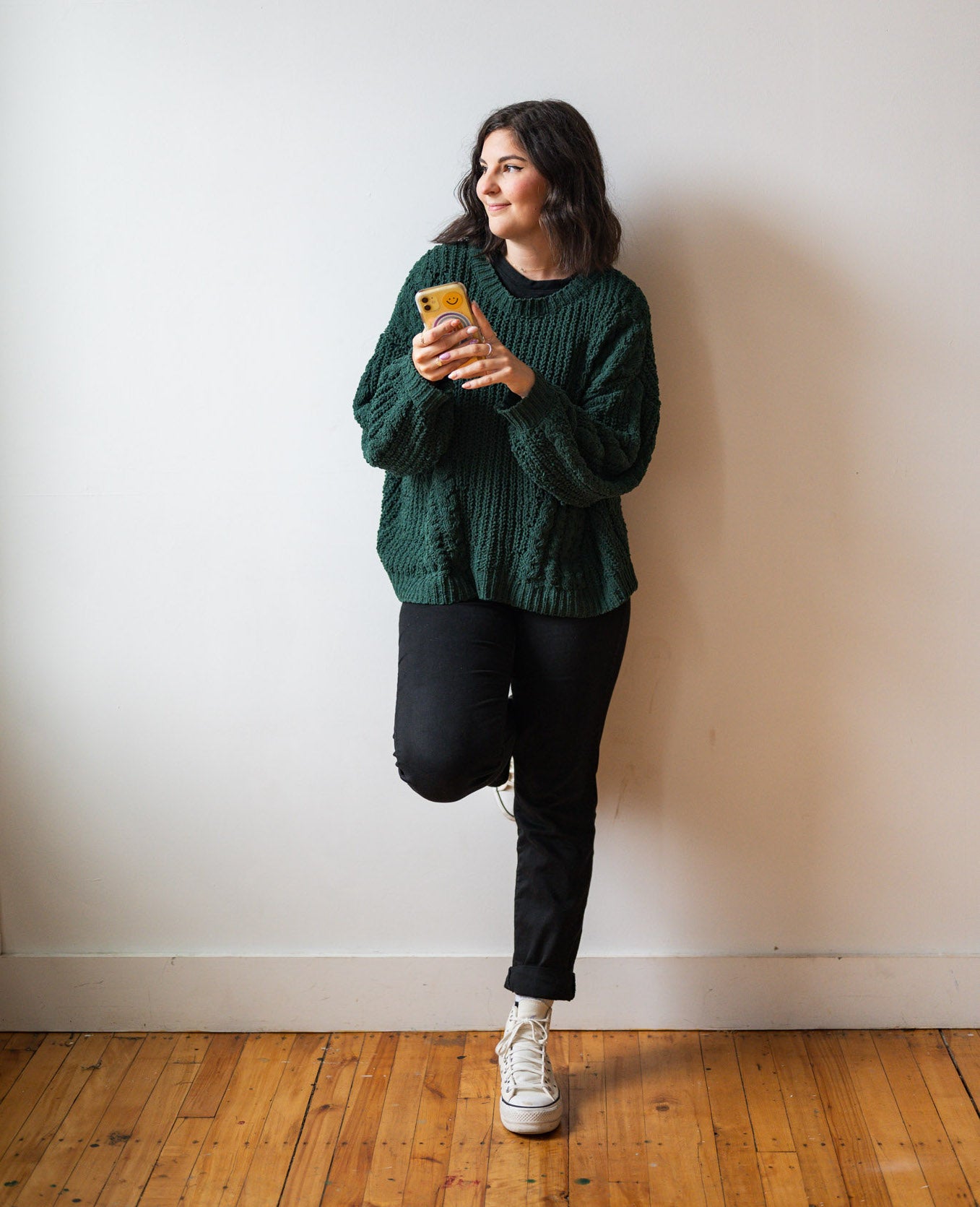 Courtney Andrews standing against a wall holding a cell phone.
