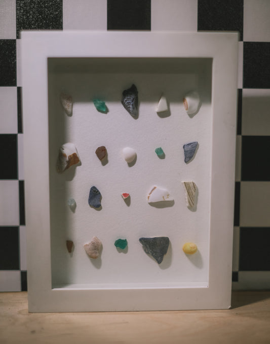 Framed display of small stones and pebbles on a checkered background