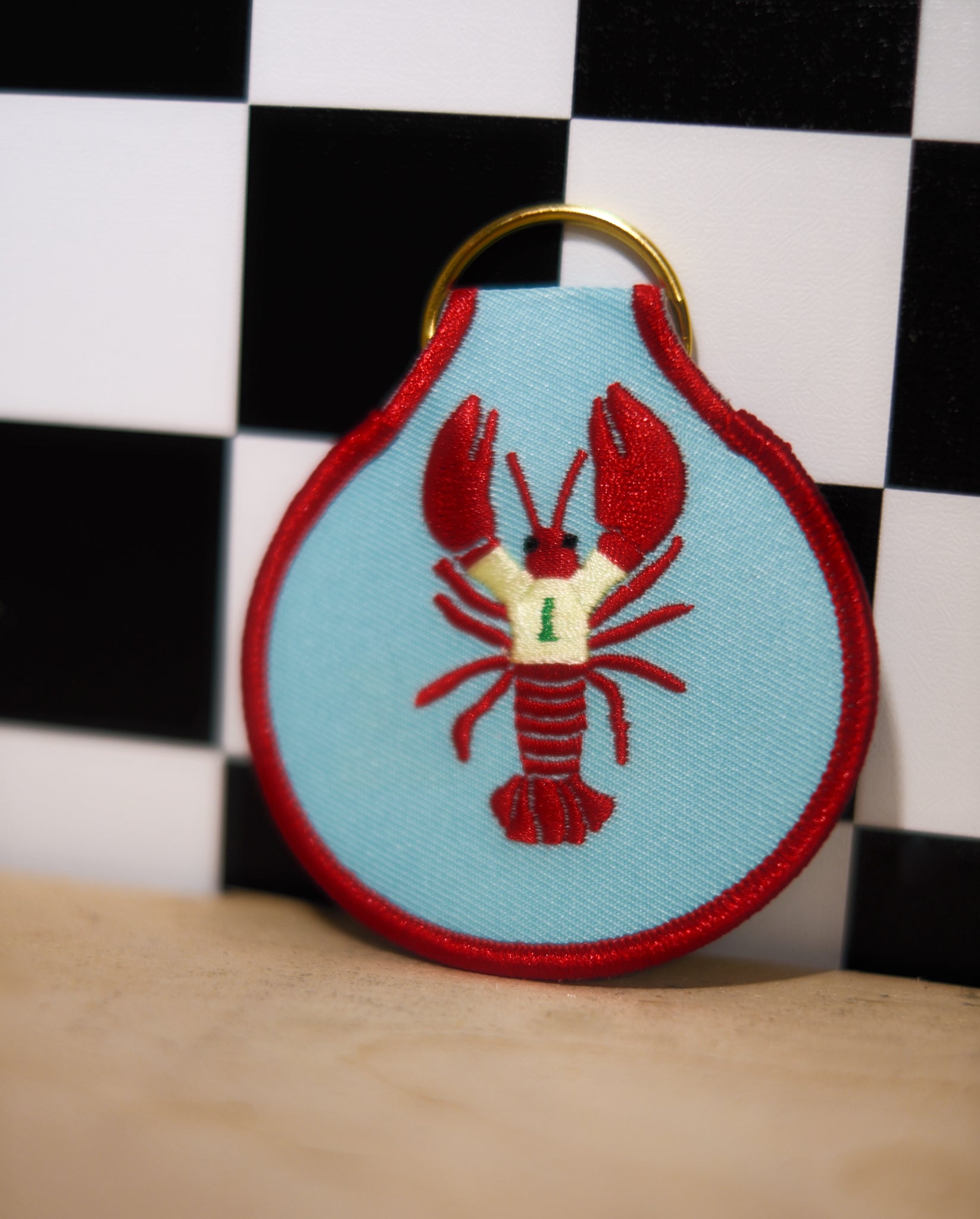 Keychain with red lobster design on a light blue background against a checkered black and white wall.