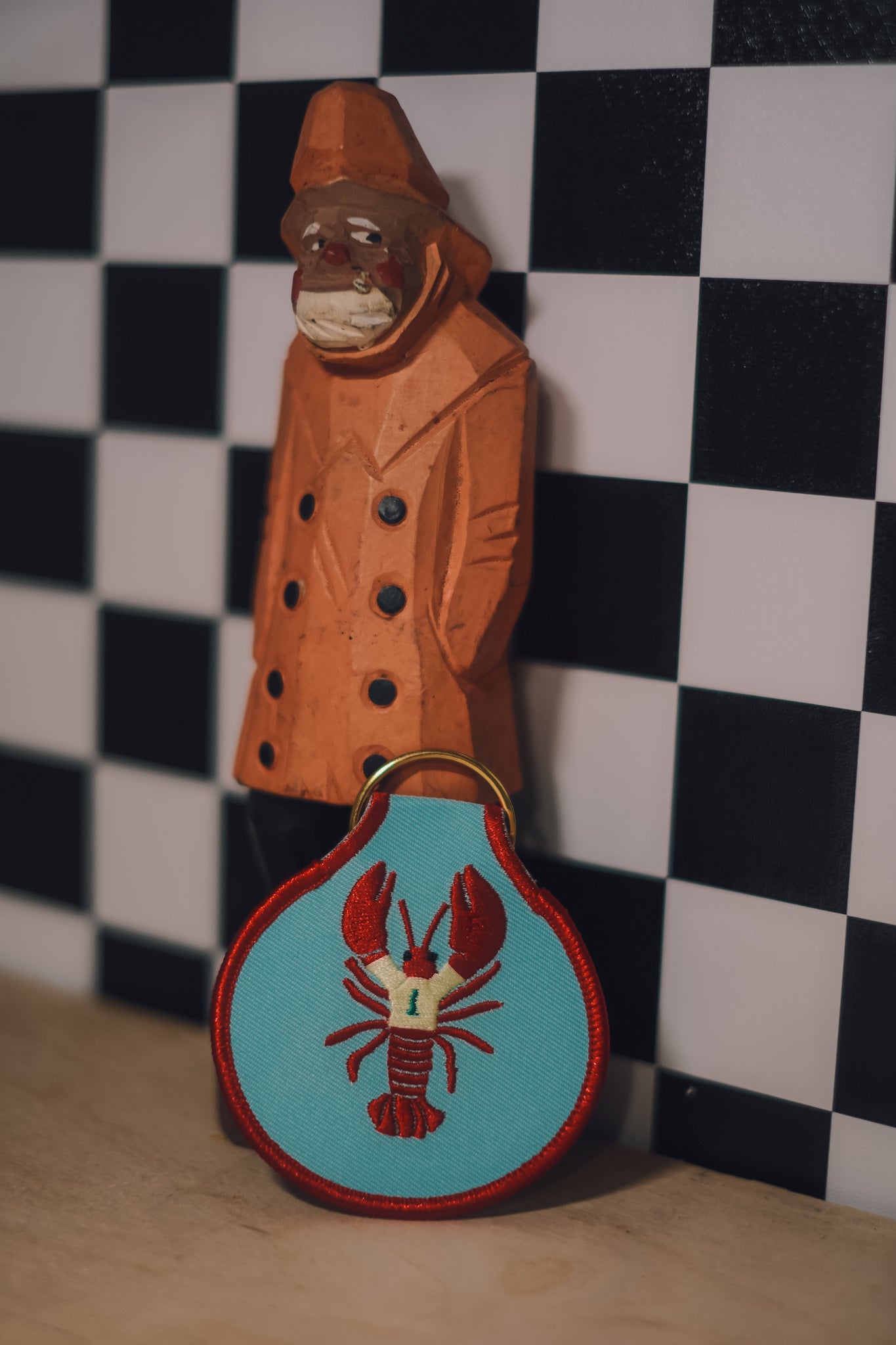 Wooden figure of a person wearing a coat with a checkered background and red lobster keychain with yellow sweater.
