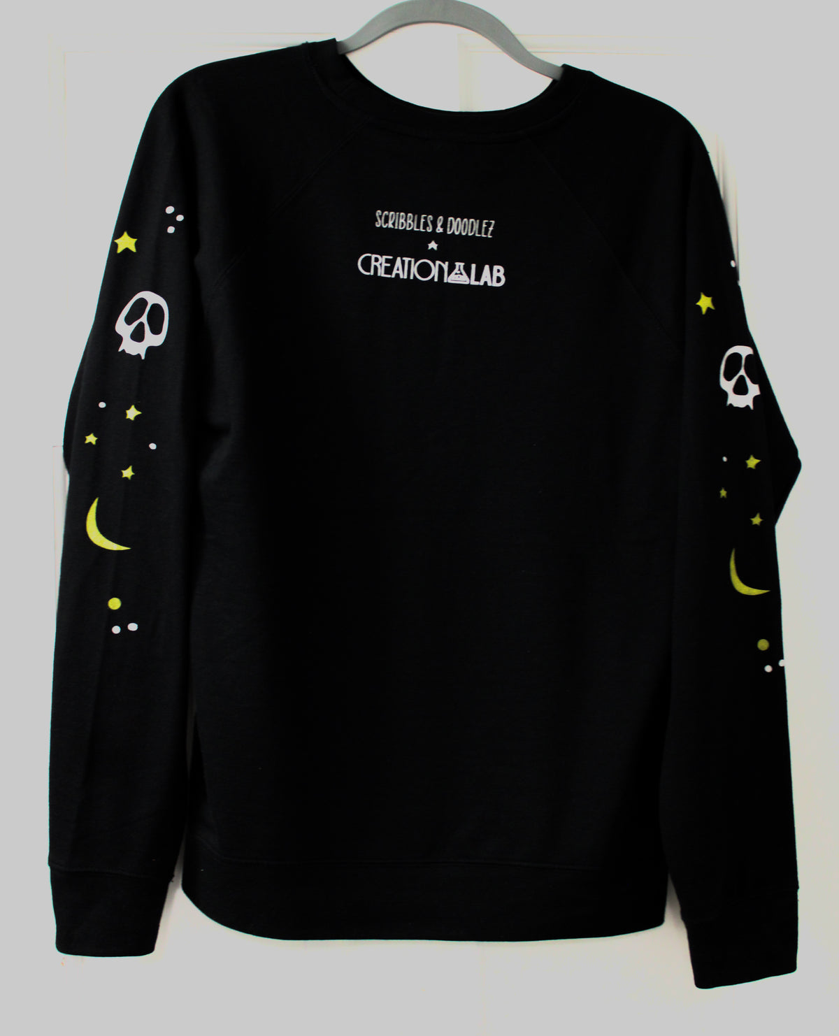 back of black crew sweatshirt featuring white dots, yellow moon and stars and white skeletons faces.