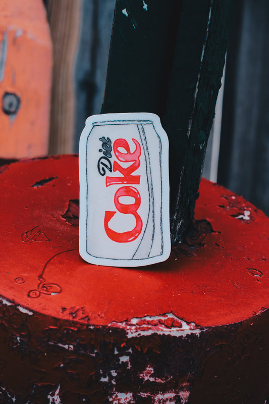 Sticker of a soda can with 'Coke' branding on a red surface.