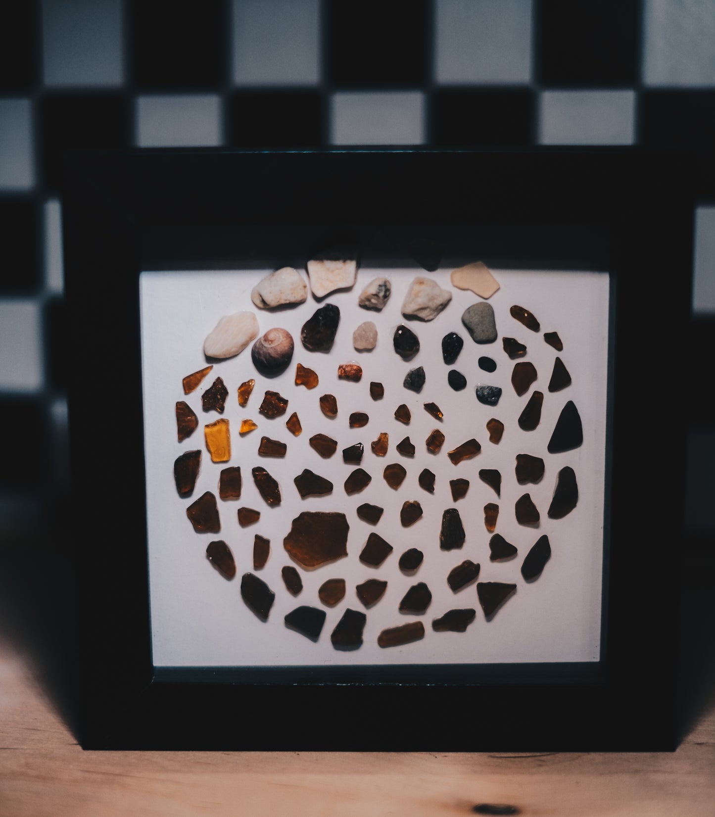 Framed artwork with a circular mosaic of stones on a white background