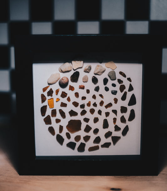 Framed artwork with a circular mosaic of stones on a white background