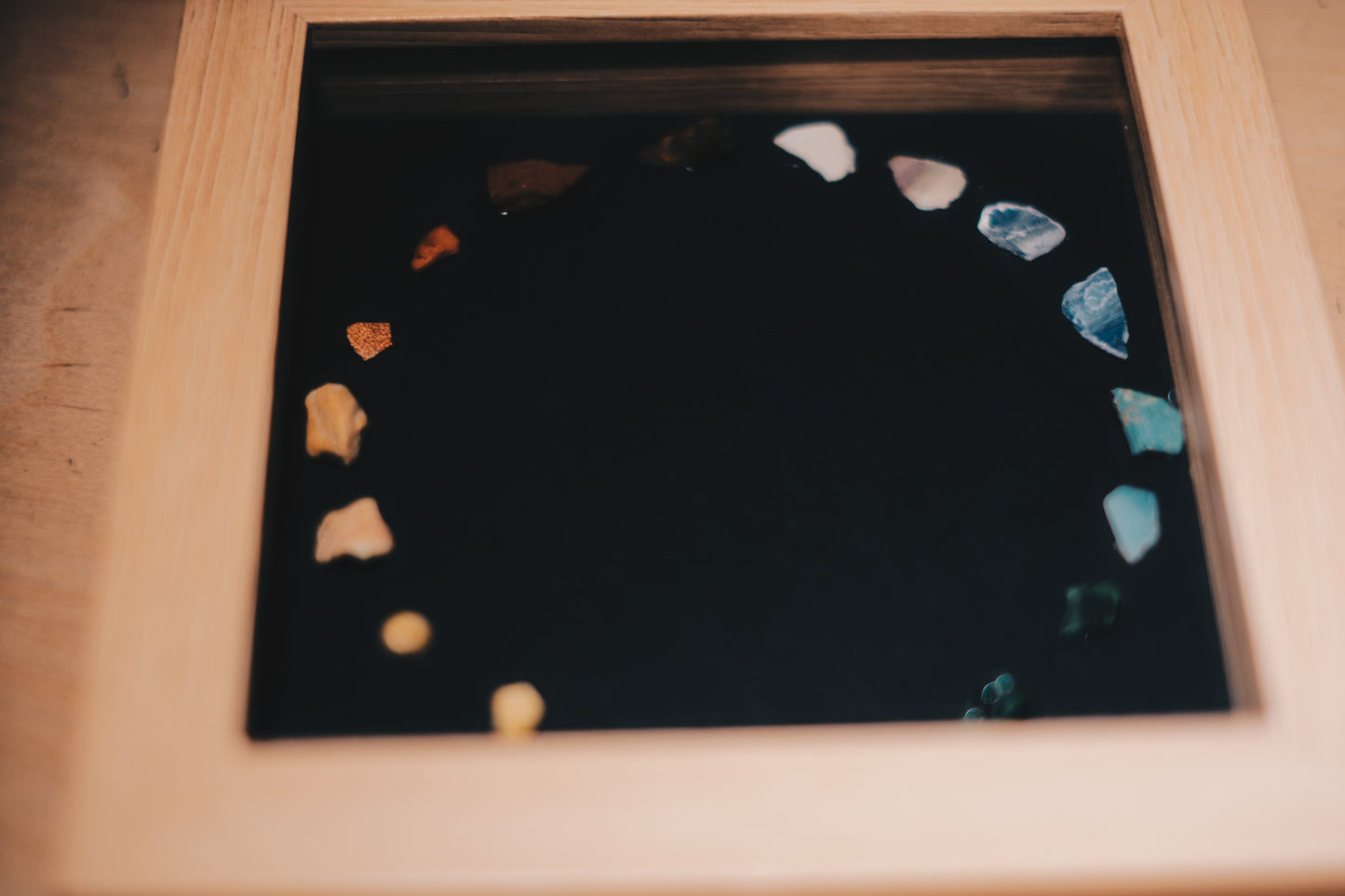 Decorative piece with colored stones on a black background in a wooden frame.