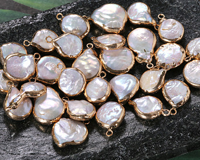 A pile of irregular baroque pearl pendants with gold-tone bezel settings, displayed on a dark textured surface.